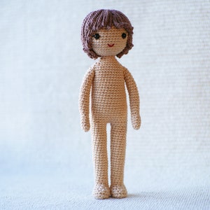May include: A crocheted doll with brown hair, a beige body, and a smiling face.
