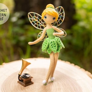 Peut inclure: Patron de crochet PDF pour une poupée de fée verte et jaune avec des ailes. La poupée est debout sur une surface en bois avec un petit gramophone.