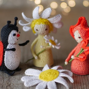 May include: Three crocheted toys: a ladybug, a daisy with a yellow center, and a red flower with a white face. The toys are made with soft yarn and have a whimsical, handmade look.