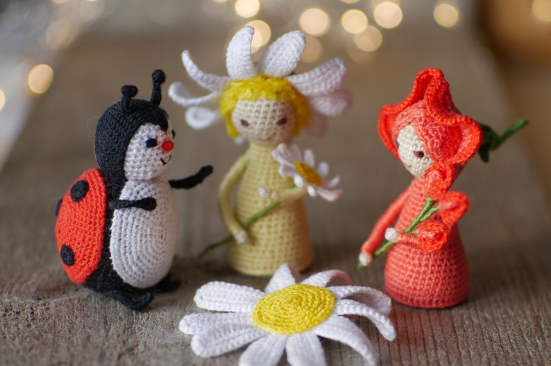 May include: Three crocheted toys: a ladybug, a daisy with a yellow center, and a red flower with a white face. The toys are made with soft yarn and have a whimsical, handmade look.