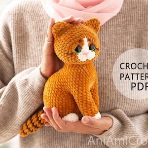 May include: A handmade orange and white crocheted cat plush toy with large dark eyes and a striped tail. The plush features a white muzzle and white paws. Text on the image reads CROCHET PATTERN PDF and AniAmiCrochet in the bottom right corner.