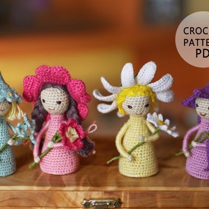 May include: Five crocheted dolls, each representing a different flower. The dolls are wearing colorful dresses and hats, and each holds a crocheted flower. The dolls are arranged in a row on a wooden surface. CROCHET PATTERN PDF