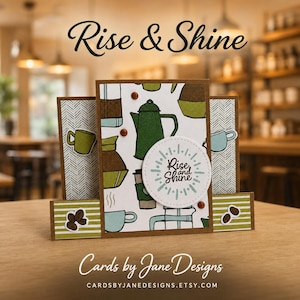 May include: A handmade greeting card featuring a coffee-themed pattern with green and blue mugs, pots, and coffee beans. A circular white die-cut overlay in the center displays the text Rise and Shine. The card has brown borders and striped accents.