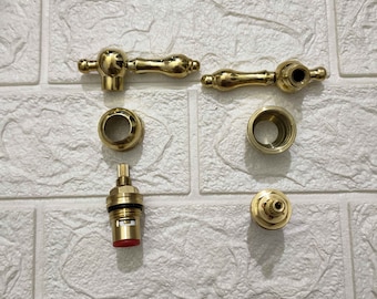 Peut inclure: Un ensemble de pièces de robinet dorées, comprenant deux poignées, deux bouchons ronds et deux petites pièces rondes avec un accent rouge.
