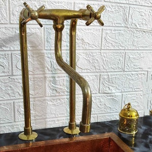 Puede incluir: Un grifo de cocina dorado con dos manijas y un caño alto. El grifo está montado en una encimera negra.