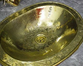 May include: A gold oval-shaped bathroom sink with an intricate floral design around the edge and a smaller floral design in the center. The sink has a drain in the center.