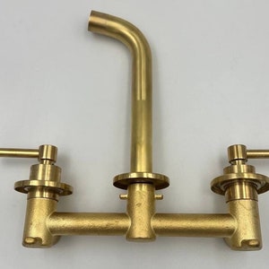 Op de afbeelding: Een gouden kraan met twee handvatten en een uitloop. De kraan is ontworpen voor een keukengoten.
