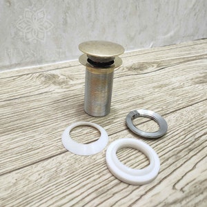 May include: A gold-toned sink drain stopper with a chrome finish. The stopper comes with three white plastic rings.