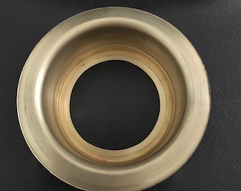 May include: A gold-colored metal ring with a raised outer edge and a smooth inner surface. The ring has a circular opening in the center.