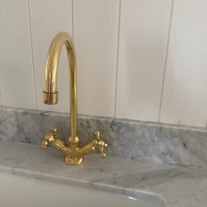 May include: A gold-toned kitchen faucet with two handles and a high-arc spout. The faucet is mounted on a white marble countertop.