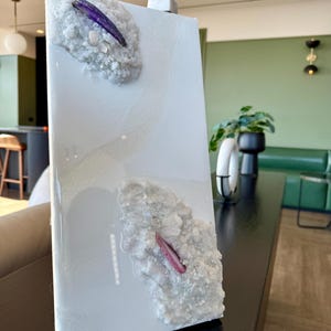 Op de afbeelding: Witte rechthoekige canvas met een textuur, wit, 3D-ontwerp. Het ontwerp bevat twee paarse en roze kristallen. De canvas is onderaan links gesigneerd met "CAMILLA ARTISTRY".