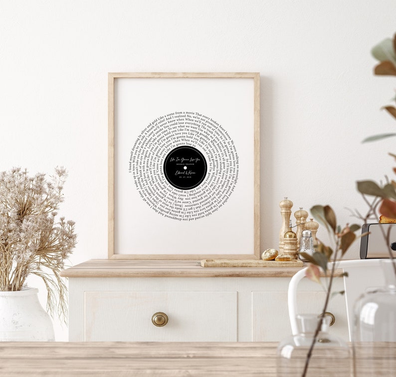 May include: Framed print featuring a black and white design resembling a vinyl record. The circular design includes song lyrics and the text "Life Is Gonna Love You" by Edward & Karen. The print is displayed in a light brown wooden frame.