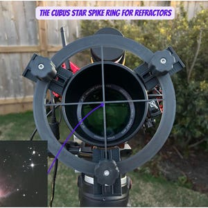 May include: A black star spike ring for refractor telescopes. The ring is attached to a telescope with a black and red body. The ring has four spokes that create a cross pattern. The image also shows a small image of a nebula in the lower left corner.