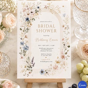 May include: A floral bridal shower invitation card. The design features an arch shape with the words "BRIDAL SHOWER" and the name "Bethany Carver". The card is decorated with watercolour flowers in shades of pink, blue, and beige. The invitation is on a small wooden easel.