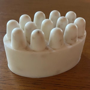 May include: White soap bar with a textured surface and multiple raised bumps. The soap bar is oval shaped.
