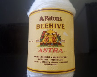 May include: A white ball of Patons Beehive Astra yarn. The label reads "Patons Beehive Astra" and includes information about the yarn being machine washable, machine dryable, mothproof, and unshrinkable.