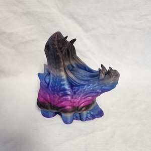 May include: A 3D printed sculpture of a dragon's head with a black, blue, and pink gradient paint finish. The dragon's mouth is open and its teeth are visible.