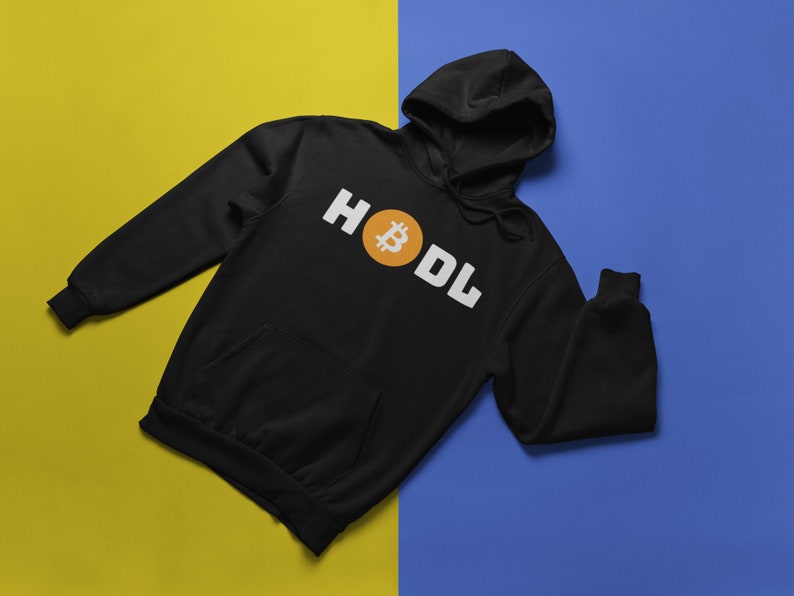 以下が含まれることがあります： 白い文字で「HODL」という言葉とオレンジ色のビットコインのシンボルが入った黒いパーカー。 パーカーにはフロントポケットとドローストリングフードが付いています。 背景は黄色と青に分かれています。