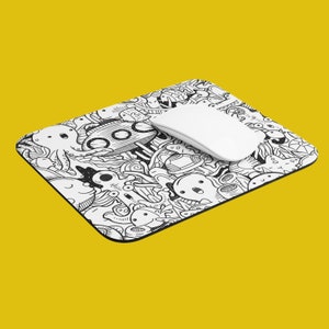 Pode incluir: Um rato de computador branco está sobre um tapete de rato com rabiscos em preto e branco. O tapete de rato apresenta uma variedade de desenhos caprichosos, incluindo um polvo, um submarino e outras criaturas marinhas.