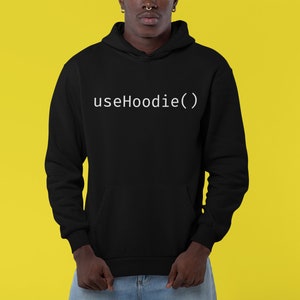 Könnte beinhalten: Ein schwarzer Hoodie mit dem Text "useHoodie()" in Weiß auf der Vorderseite.