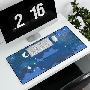 May include: A rectangular desk mat with a night sky design, featuring clouds, stars, and a crescent moon in blue and white. A white keyboard and mouse are on the mat, with a computer monitor in the background.