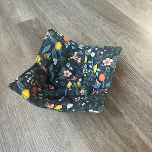 May include: A dark blue fabric bowl with a floral pattern featuring lemons, flowers, and leaves. The bowl is quilted and has a soft texture.