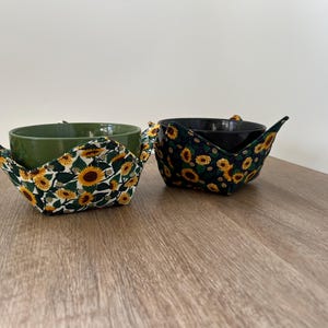 May include: Two bowls with sunflower print fabric bowl cozies. One bowl is green and the other is black.