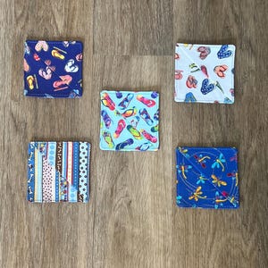 May include: Five fabric coasters with different patterns. The coasters are square and feature a variety of designs, including flip flops, dragonflies, and stripes.