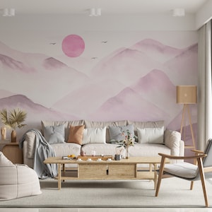 May include: A living room interior design with a light grey sofa, a wooden coffee table, a grey armchair, and a floor lamp. The wall features a watercolor painting of pink mountains and a pink sun.