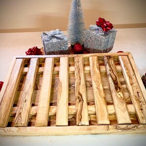 May include: A rectangular wooden serving tray with a slatted design. The tray is made of light-coloured wood with a natural grain pattern. The tray is surrounded by Christmas decorations, including baubles and wrapped gifts.