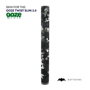 Könnte beinhalten: Eine schwarze und silberne Tarnhaut für den Ooze Twist Slim 2.0 Vape-Stift. Die Haut besteht aus einem strapazierfähigen Material und verfügt über ein einzigartiges Tarnmuster. BATTSKINS ist auf der Unterseite der Haut aufgedruckt.