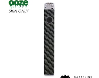Op de afbeelding: Een zwarte en grijze carbonfiber-huid voor een vape-apparaat. De huid is ontworpen om te passen op het vape-apparaat van het merk Ooze. De huid is gelabeld met "SKIN ONLY" en "BATTSKINS".