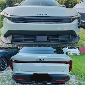 以下が含まれることがあります： ライトグレーのKia EV6電気自動車、前面と背面からのビュー。前面にはKiaのロゴ、黒いグリル、ヘッドライトが表示されています。背面にはKiaのロゴとテールライトが表示されています。車は芝生の上に駐車されています。