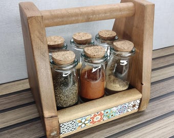 以下が含まれることがあります： コルクの蓋が付いた6つのガラス瓶が入った木製のスパイスラック。瓶には様々なスパイスが入っており、ラックの下部には装飾的なタイルのストリップが付いています。持ち運びしやすいようにハンドルが付いています。