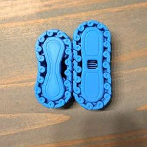 May include: Two bright blue plastic chain-link style connectors with a textured, scalloped edge. The smaller connector has a smooth, solid center, while the larger connector features a central rectangular opening with a small grid pattern.