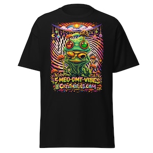 Puede incluir: Camiseta negra con un gráfico colorido de una rana verde y setas. El diseño incluye el texto "5-MEO-DMT-VIBES" y "CATSNDRUGS.COM" en un estilo psicodélico. La camiseta está hecha de un material suave.