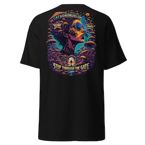 Könnte beinhalten: Schwarzes T-Shirt mit einem lebendigen Grafikdesign. Das Design zeigt ein stilisiertes Porträt einer Person mit Sonnenbrille, umgeben von Pilzen und dem Text "STEP THROUGH THE GATE". Die Website "CATSONDRUGS.COM" ist ebenfalls abgebildet.