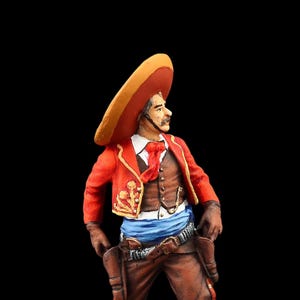 May include: A painted figurine of a man wearing a red and gold sombrero, a red jacket with gold embroidery, a blue sash, and brown pants. He is holding a gun in his right hand.