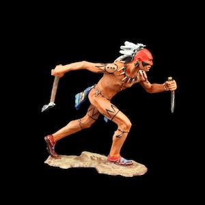 May include: A hand-painted figurine of a Native American warrior running with a tomahawk in one hand and a knife in the other. The warrior is wearing a feathered headdress and has red and black paint on his face.