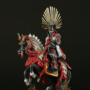 Puede incluir: Una figurita miniatura pintada a mano de un guerrero samurái a caballo. El guerrero lleva una armadura tradicional y un casco con una cresta dorada. El caballo está adornado con una armadura roja y dorada elaborada. La figurita está colocada sobre una base de madera.