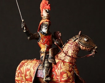 Peut inclure: Une figurine miniature détaillée d'un chevalier à cheval, portant une armure rouge et or avec un casque à plumes rouge et or. Le cheval est également orné d'une armure à motifs rouge et or.