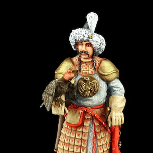 Puede incluir: Figura detallada de un guerrero con armadura ornamentada, sosteniendo un ave rapaz. La figura lleva un sombrero de piel con una pluma, hombreras doradas y botas rojas. La armadura está detallada con un emblema dorado y detalles rojos.