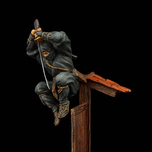 Puede incluir: Una figura de ninja negra con una espada, saltando desde una estructura de madera con un techo rojo. La figura está en el aire, con una pierna extendida y la otra doblada. La figura está de pie sobre una base circular con un patrón de cuadros.