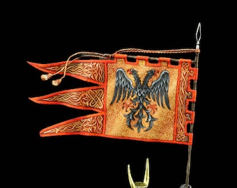May include: A hand-painted pewter figurine of a knight in armor holding a flag with a double-headed eagle. The knight is wearing a yellow and red tunic and a helmet with horns. The flag is red, gold, and black with a double-headed eagle in the center.