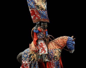 May include: A miniature figure of a knight on horseback, wearing armor and a red and blue cape. The knight is holding a flag with a lion design. The horse is also decorated with a lion design.