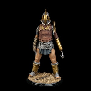 Puede incluir: Una figurita miniatura pintada de un gladiador romano que lleva un casco con detalles dorados, una armadura de malla y una falda corta. El gladiador sostiene un arma con un gancho en el extremo. La figurita está de pie sobre una pequeña base redonda.