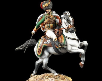 May include: A detailed figurine of a mounted soldier in a green and gold uniform, holding a sword. The white horse has a patterned saddle and is rearing up on its hind legs. The base is a textured, tan-colored rock.