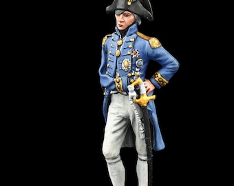 May include: A painted figurine of a man in a blue and gold military uniform with a black hat and white pants. He is holding a sword and standing on a wooden base.