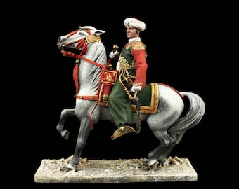May include: A painted figurine of a man on horseback wearing a red and green uniform with a white turban. The horse is white with gold trim and a red tassel. The figurine is on a brown base.