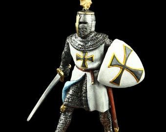 May include: A miniature knight figurine, clad in chainmail and a white tunic with a black cross emblem. The knight holds a sword and a shield with a matching cross design. The figure stands on a textured, tan base against a black backdrop.